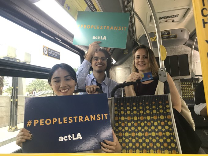 Three smiling people sitting in a bus with signs that say Peoples Transit