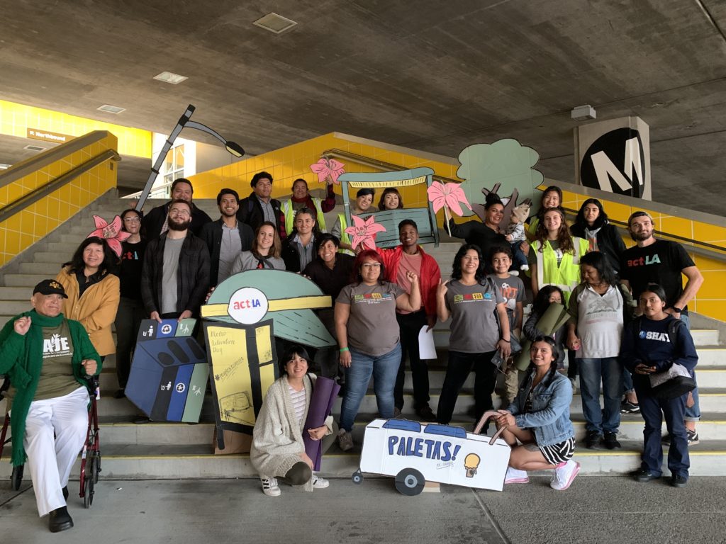 A group of smiling people in front of a Metro station with various posters