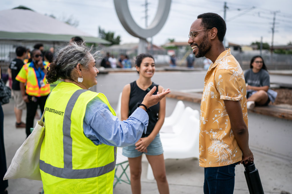 An ACT L.A. member in a neon safety vest smiling and talking to two people